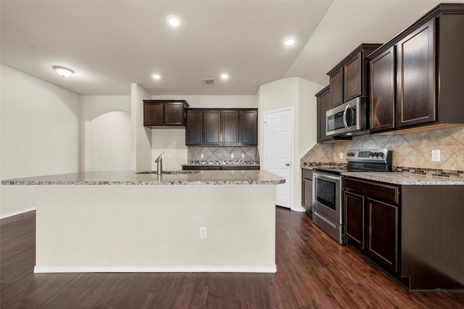 Kitchen with appliances with stainless steel finishes, light stone counters, dark brown cabinets, an island with sink, and dark wood-style floors | Image 13