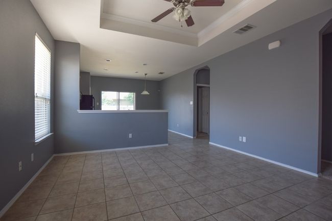 Tiled empty room with arched walkways, ceiling fan, a tray ceiling, baseboards, and ornamental molding | Image 34