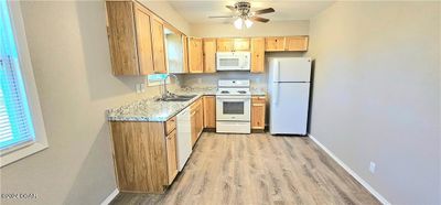 Kitchen with light stone countertops, sink, light hardwood / wood-style floors, white appliances, and ceiling fan | Image 3