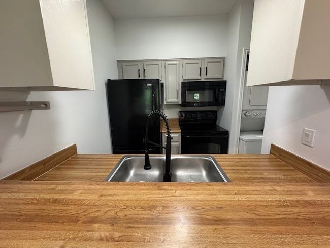 Kitchen with black appliances, stacked washer / dryer, light countertops, and gray cabinetry | Image 12