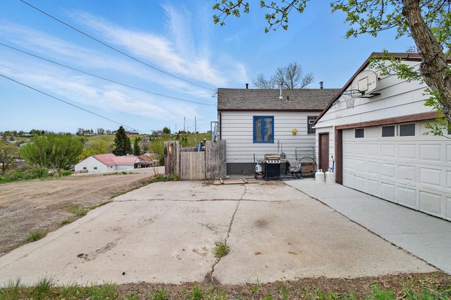 Back of house with a garage, fence, concrete driveway, an outbuilding, and roof with shingles | Image 34