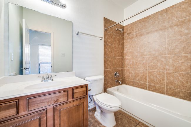 This well-appointed secondary bathroom offers warm wood cabinetry that provides ample storage and a touch of natural elegance. A tiled bath/shower combination adds durability and style, while the mounted mirror above the vanity enhances light and functionality. Designed for comfort and convenience, it’s a perfect blend of practicality and timeless design. | Image 15