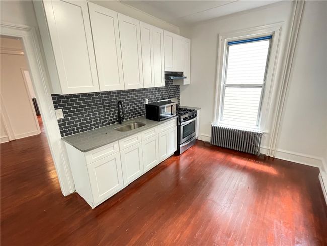 Kitchen with radiator, a sink, under cabinet range hood, stainless steel gas range, and dark wood-style flooring | Image 10