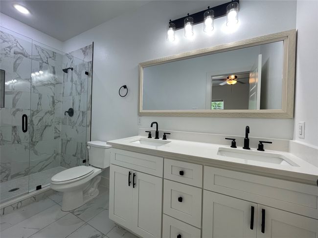 Bathroom with marble finish flooring, a marble finish shower, toilet, double vanity, and a ceiling fan | Image 26