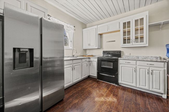 Kitchen with wood ceiling, white cabinets, stainless steel fridge, and electric range | Image 9