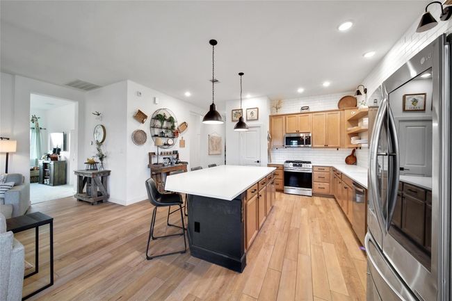 This modern kitchen features stainless steel appliances, light wood cabinets, and a large island with seating. The open layout and hardwood floors create a warm, inviting atmosphere. | Image 20