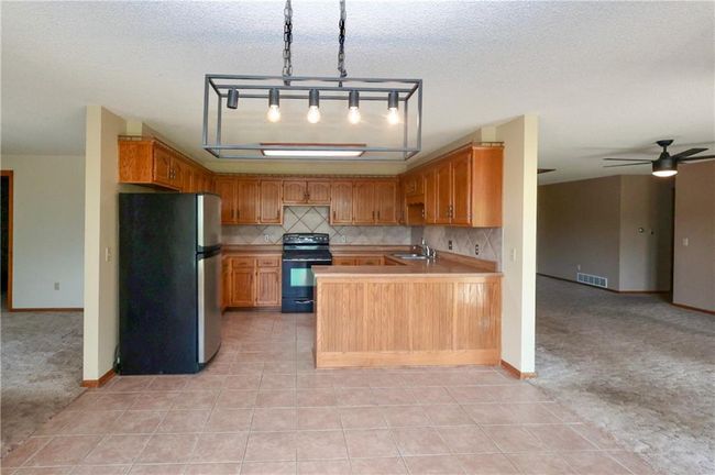 Kitchen featuring freestanding refrigerator, black electric range, open floor plan, light countertops, and a ceiling fan | Image 17