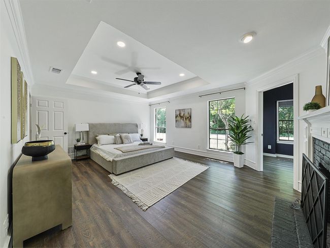 Bedroom featuring dark wood-style floors, a brick fireplace, a tray ceiling, and visible vents | Image 11