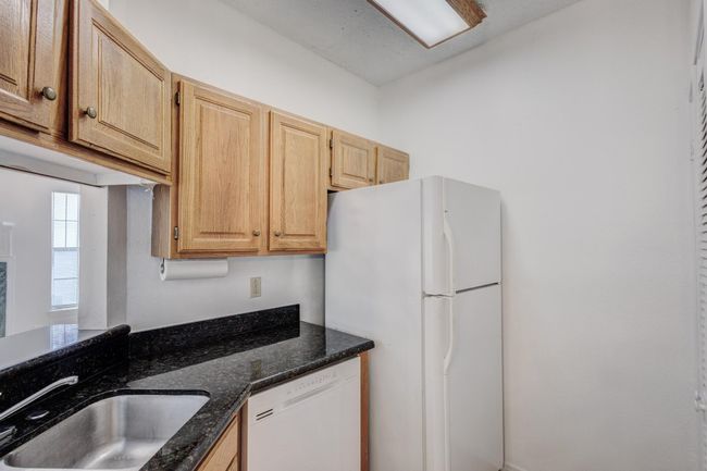 Kitchen featuring white appliances, a sink, dark stone counters, and light brown cabinets | Image 6