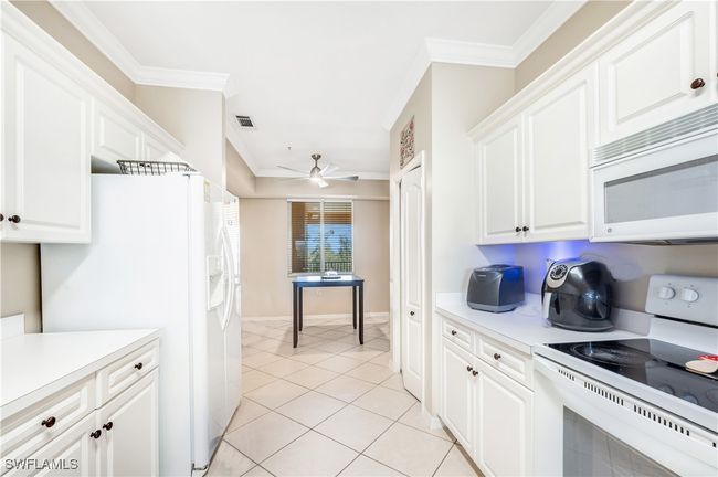 Kitchen with white appliances, ceiling fan, white cabinets, crown molding, and light tile patterned floors | Image 8