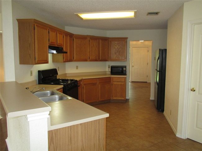 Kitchen with brown cabinetry, black appliances, light countertops, a peninsula, and under cabinet range hood | Image 5
