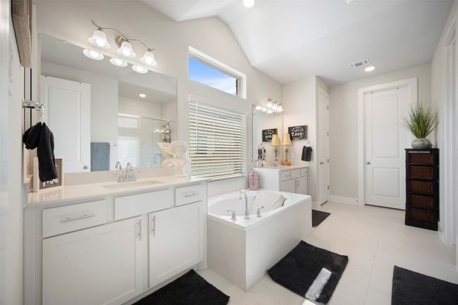 Full bath featuring a shower stall, lofted ceiling, a bath, two vanities, and tile patterned floors | Image 25