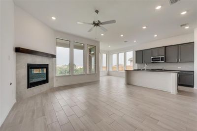 Kitchen featuring an island with sink, light wood-type flooring, a fireplace, and ceiling fan | Image 3