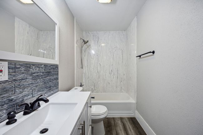 Bathroom with bathing tub / shower combination, vanity, dark wood-type flooring, a textured wall, and backsplash | Image 10