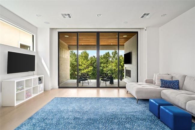 The third-floor media lounge is the ultimate retreat—perfect for movie nights, playtime, or laid-back lounging. Wall-to-wall glass doors open to a covered terrace with treetop views and a fireplace, seamlessly blending indoor comfort with outdoor serenity. | Image 27