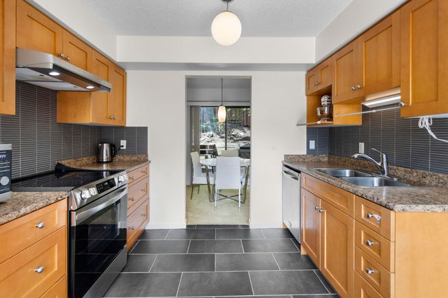 Kitchen with under cabinet range hood, appliances with stainless steel finishes, backsplash, brown cabinetry, and a textured ceiling | Image 13