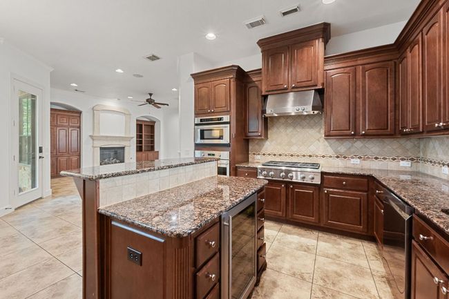 Kitchen featuring wine cooler, under cabinet range hood, appliances with stainless steel finishes, a center island, and ceiling fan | Image 17