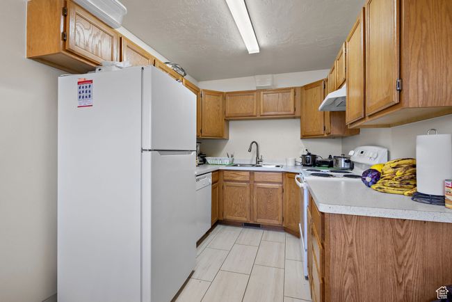Kitchen with white appliances, under cabinet range hood, light countertops, and brown cabinetry | Image 25