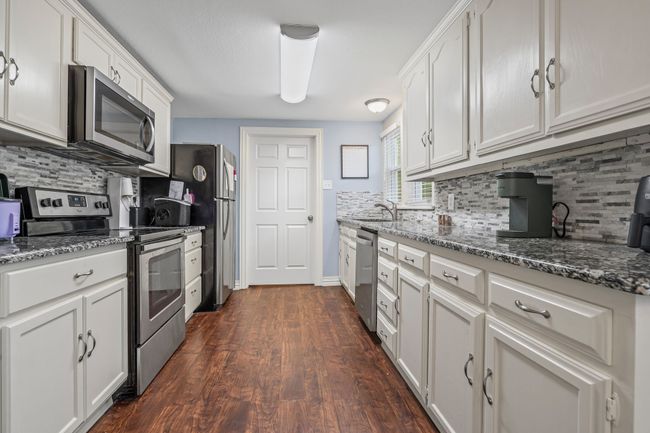 Kitchen with appliances with stainless steel finishes, backsplash, white cabinets, and dark wood finished floors | Image 12