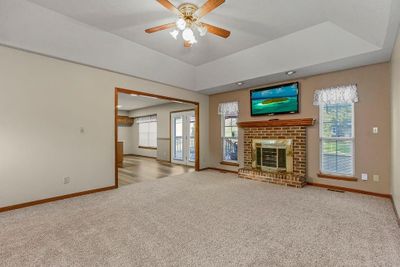 Unfurnished living room featuring light carpet, ceiling fan, a fireplace, and a healthy amount of sunlight | Image 3