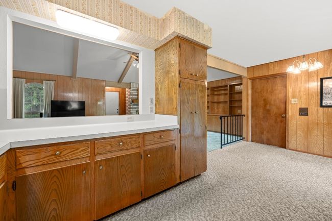 Kitchen featuring wood walls, light carpet, light countertops, brown cabinetry, and a chandelier | Image 12