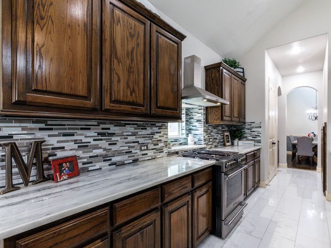 A look at the stylish tile backsplash and the pantry and wine fridge located in the kitchen hallway. | Image 13