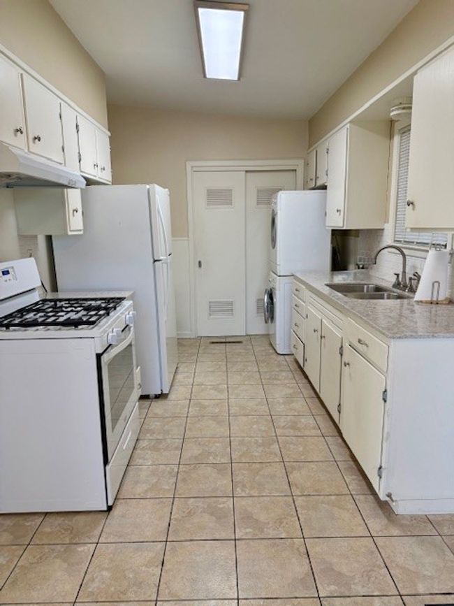 Kitchen featuring light tile patterned flooring, stacked washer / drying machine, a sink, and white appliances | Image 20