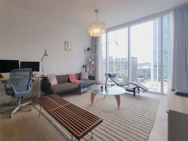 Living area with a desk, wood finished floors, floor to ceiling windows, and a city view | Image 8