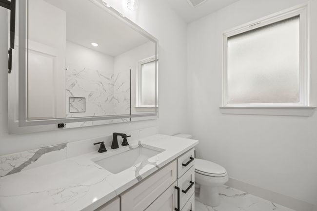 Bathroom with marble look tiles, vanity, toilet, and baseboards | Image 25
