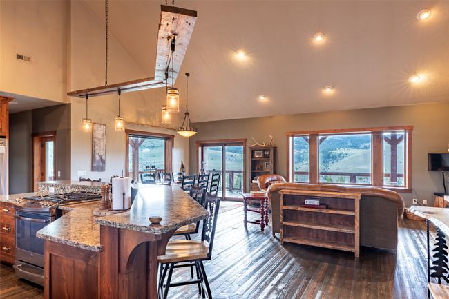 Kitchen with stainless steel gas range oven, high vaulted ceiling, dark wood finished floors, light stone counters, and a kitchen bar | Image 7