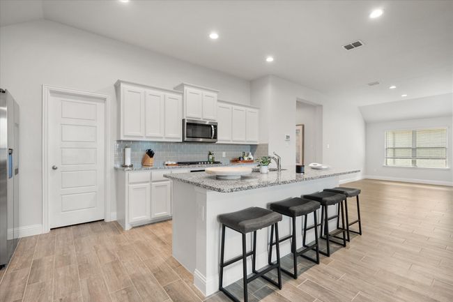 Kitchen featuring stainless steel appliances, light wood finished floors, tasteful backsplash, a center island with sink, and white cabinets | Image 8