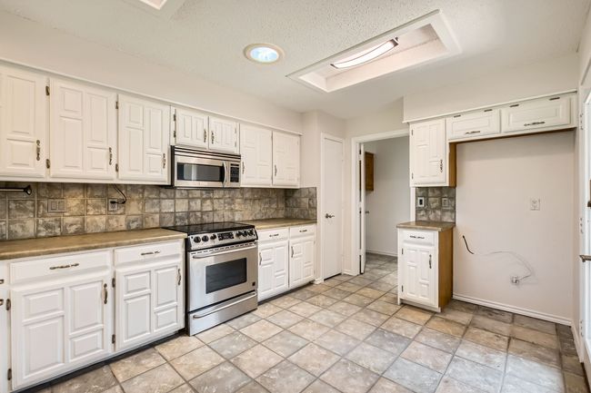 Kitchen featuring stainless steel appliances, decorative backsplash, white cabinets, and light countertops | Image 6