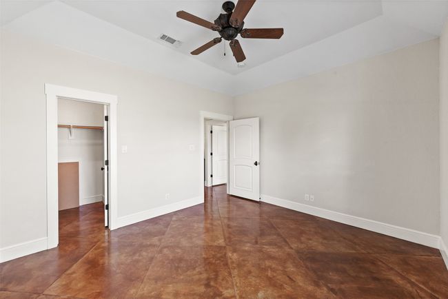 Unfurnished bedroom with concrete flooring, a walk in closet, baseboards, a closet, and a high ceiling | Image 24