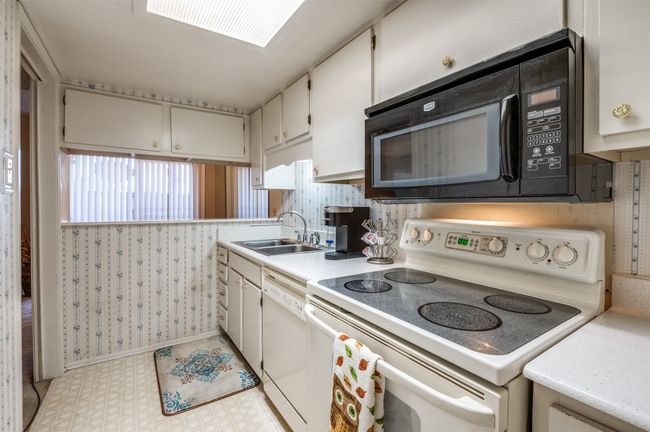 Kitchen with white appliances, wallpapered walls, light flooring, light countertops, and white cabinetry | Image 9