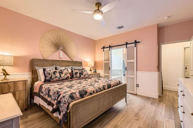 Bedroom with a barn door, wainscoting, light wood-type flooring, and a ceiling fan | Image 15