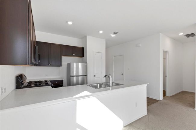 Kitchen with freestanding refrigerator, range with gas stovetop, a peninsula, dark brown cabinets, and light countertops | Image 7
