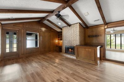 Unfurnished living room with ceiling fan with notable chandelier, a fireplace, and a textured ceiling | Image 2