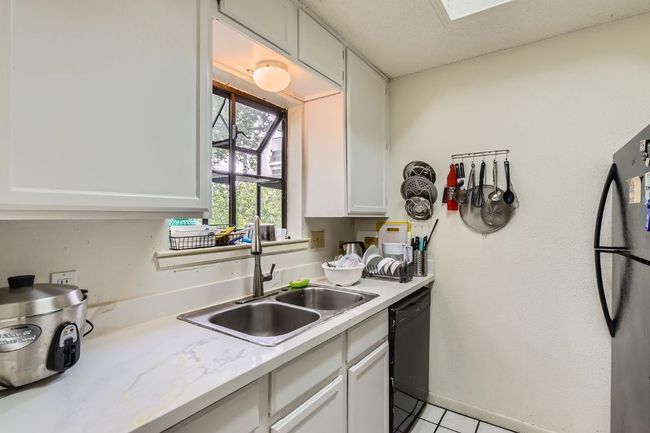 Kitchen featuring black dishwasher, light countertops, white cabinets, a sink, and light tile patterned flooring | Image 13