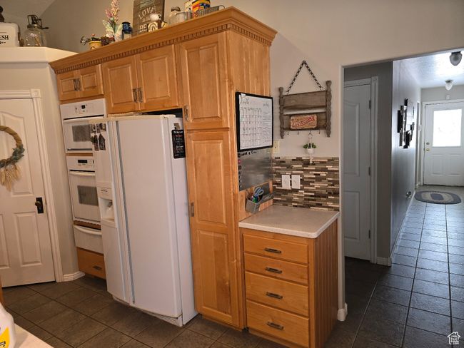 Kitchen featuring baseboards, light countertops, a warming drawer, white refrigerator with ice dispenser, and decorative backsplash | Image 22