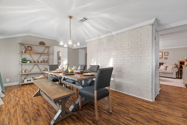 Dining area featuring brick wall, wood finished floors, a chandelier, crown molding, and lofted ceiling | Image 17