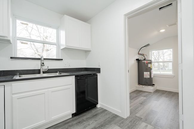 Kitchen with visible vents, dishwasher, dark countertops, electric water heater, and a sink | Image 12