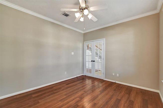 This room features warm hardwood floors, neutral walls, a ceiling fan, and elegant French doors, offering a bright and versatile space perfect for a home office or study. | Image 9