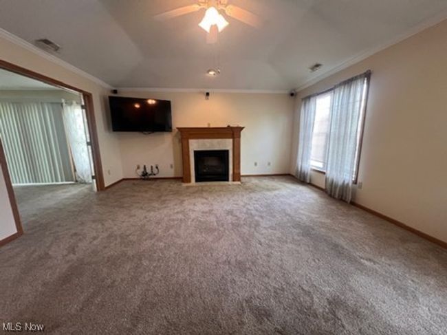 Unfurnished living room featuring crown molding, carpet flooring, ceiling fan, and a fireplace with flush hearth | Image 7
