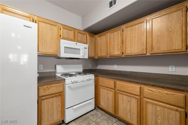 Kitchen featuring light tile patterned floors, dark countertops, visible vents, and white appliances | Image 16