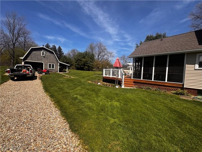 View of yard featuring an outdoor structure, a sunroom, a wooden deck, and a garage | Image 39