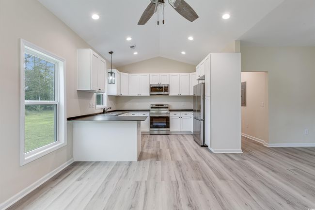 Kitchen featuring stainless steel appliances, dark countertops, light wood-style flooring, vaulted ceiling, and recessed lighting | Image 8