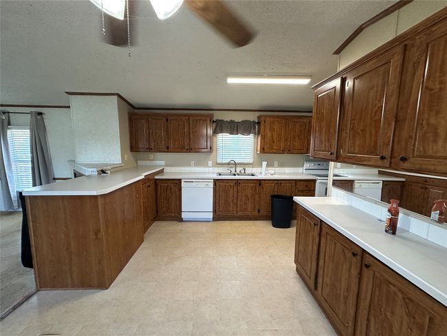 Kitchen with white appliances, a peninsula, a ceiling fan, light countertops, and a textured ceiling | Image 12
