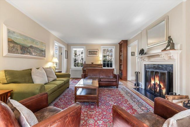 Living area featuring ornamental molding, radiator heating unit, wood finished floors, and a high end fireplace | Image 5