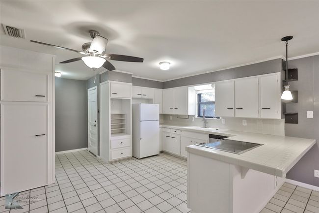 Kitchen featuring kitchen peninsula, ceiling fan, white refrigerator, decorative light fixtures, and white cabinetry | Image 5