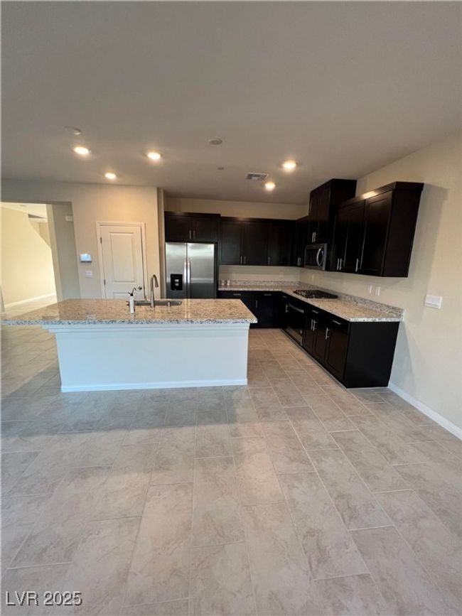 Kitchen featuring stainless steel appliances, light stone counters, dark cabinets, a kitchen island with sink, and recessed lighting | Image 7